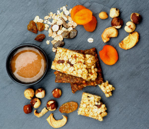 Arrangement of Useful Granola Bars with Muesli, Nuts, Dried Apricots and Bowl of Honey closeup on Black Stone background. Top View